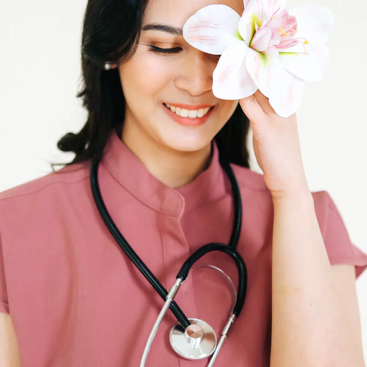 A Kindred OBGYN in pink scrubs, smiling, holding a lily over one eye